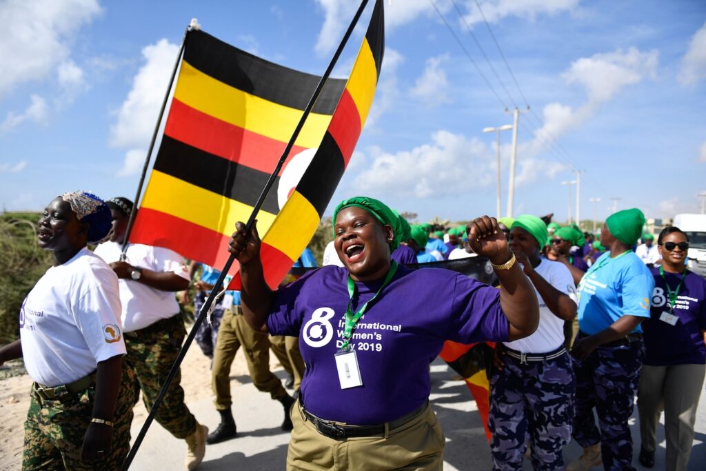 Foto de una mujer negra con la boca abierta, levantando la mano izquierda con un puño y aguantando una bandera con la otra. Forma parte de una marcha con otras mujeres negras.