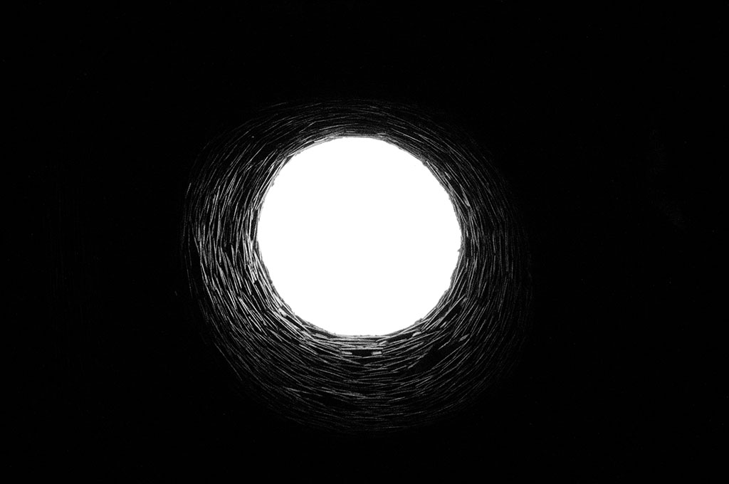 Black and white photo capturing a beam of light illuminating a well as seen from the bottom